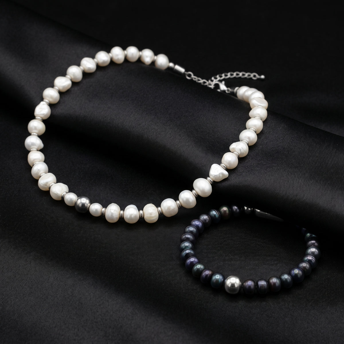 An ALFABEADS white pearl choker and dark pearl bracelet on black fabric