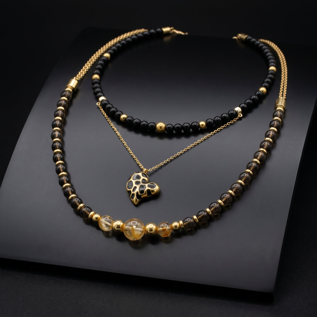Two ALFABEADS necklaces with a gold heart pendant and citrine on a dark display slab