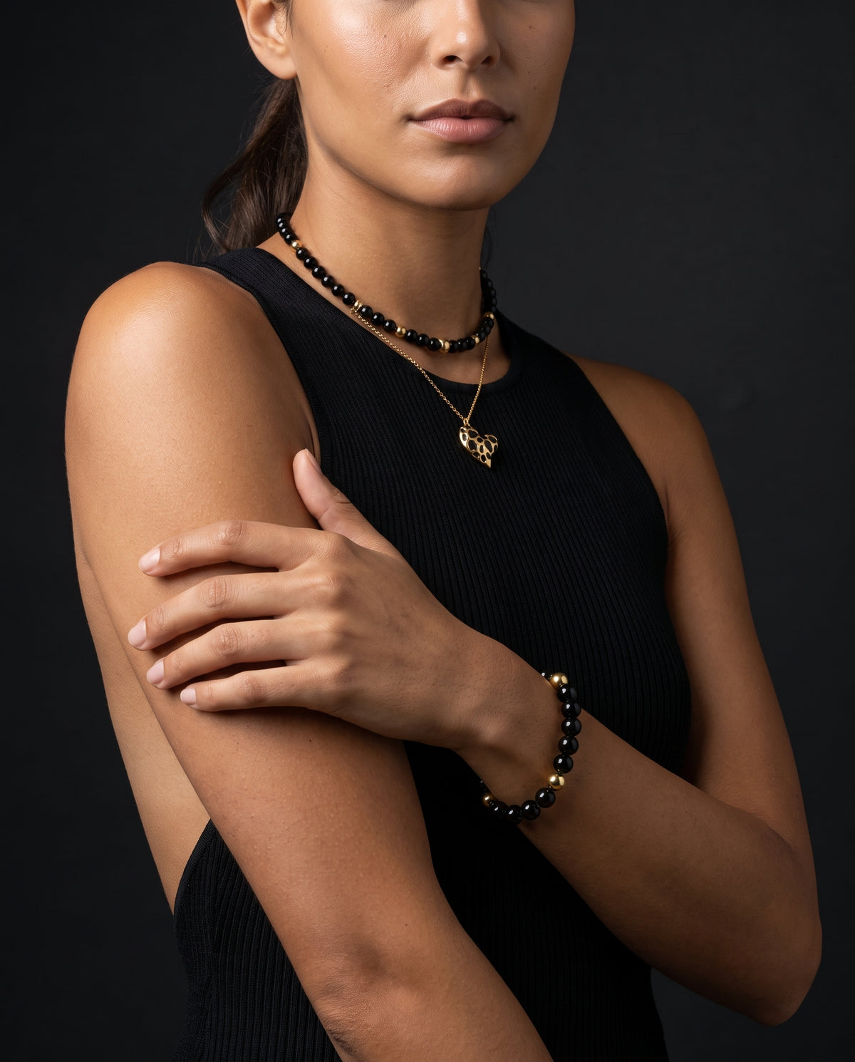 Model wearing an Alfabeads Onyx and Black Tourmaline choker with a gold heart pendant and matching bracelet with a black dress